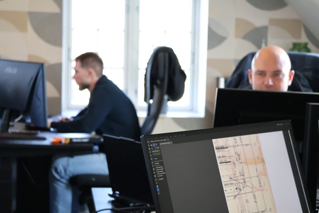 Ingeniører arbejder ved computere med tekniske tegninger og rådgivning om byggeprojekter.